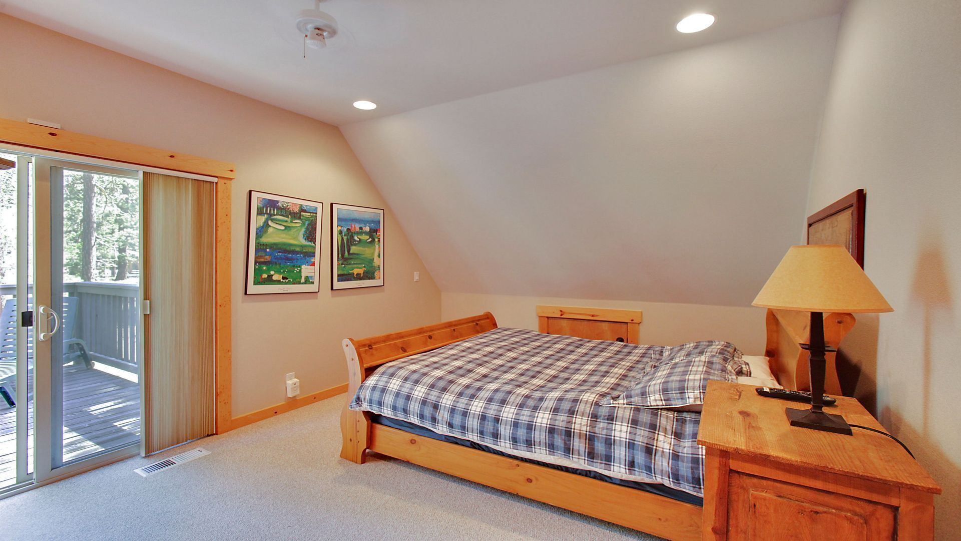 A bedroom with a wooden bed, a desk with a lamp, and a sliding glass door leading to an outdoor area.