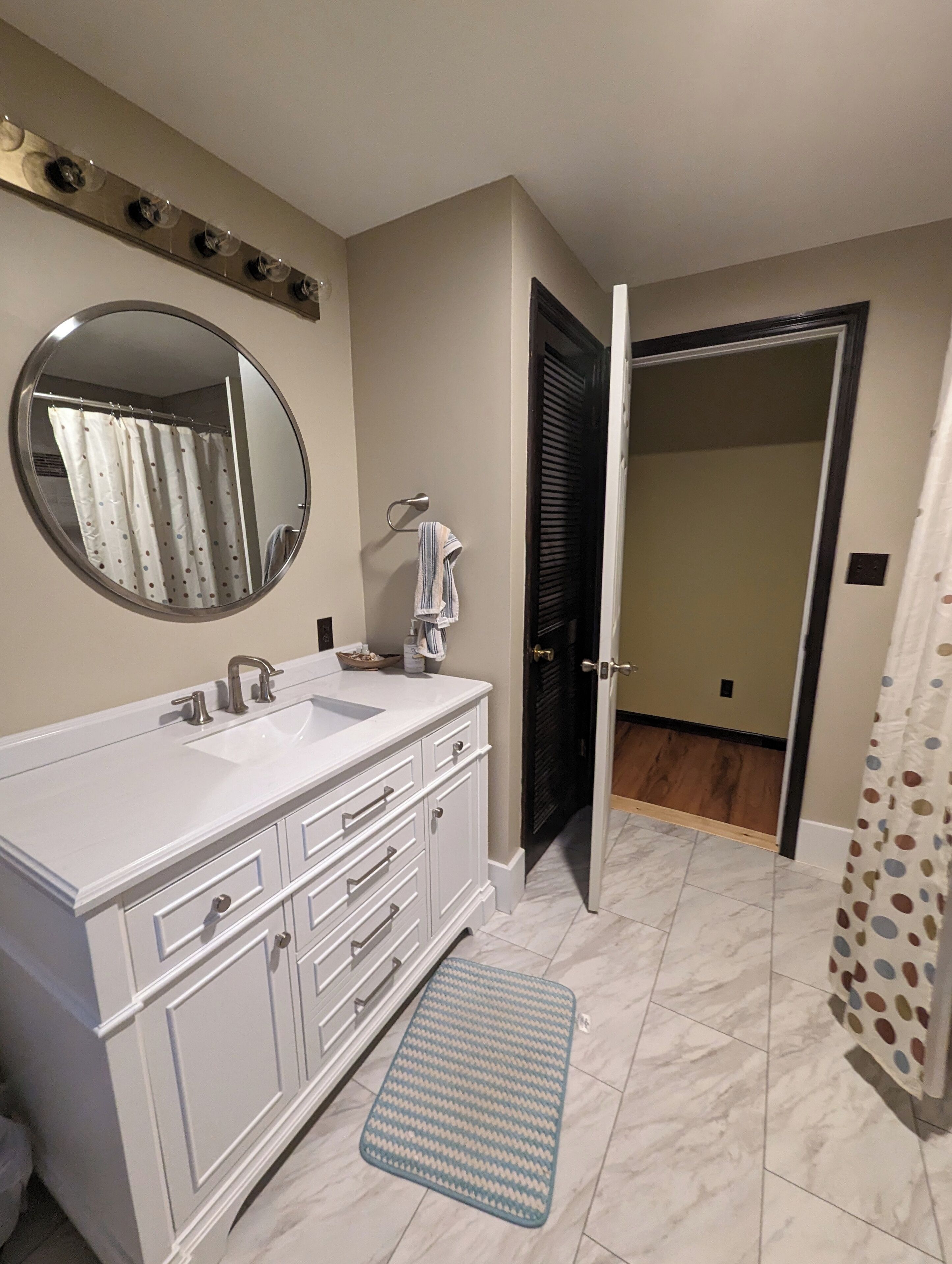 A bathroom with a white vanity, a round mirror, a towel rack, and a shower curtain.