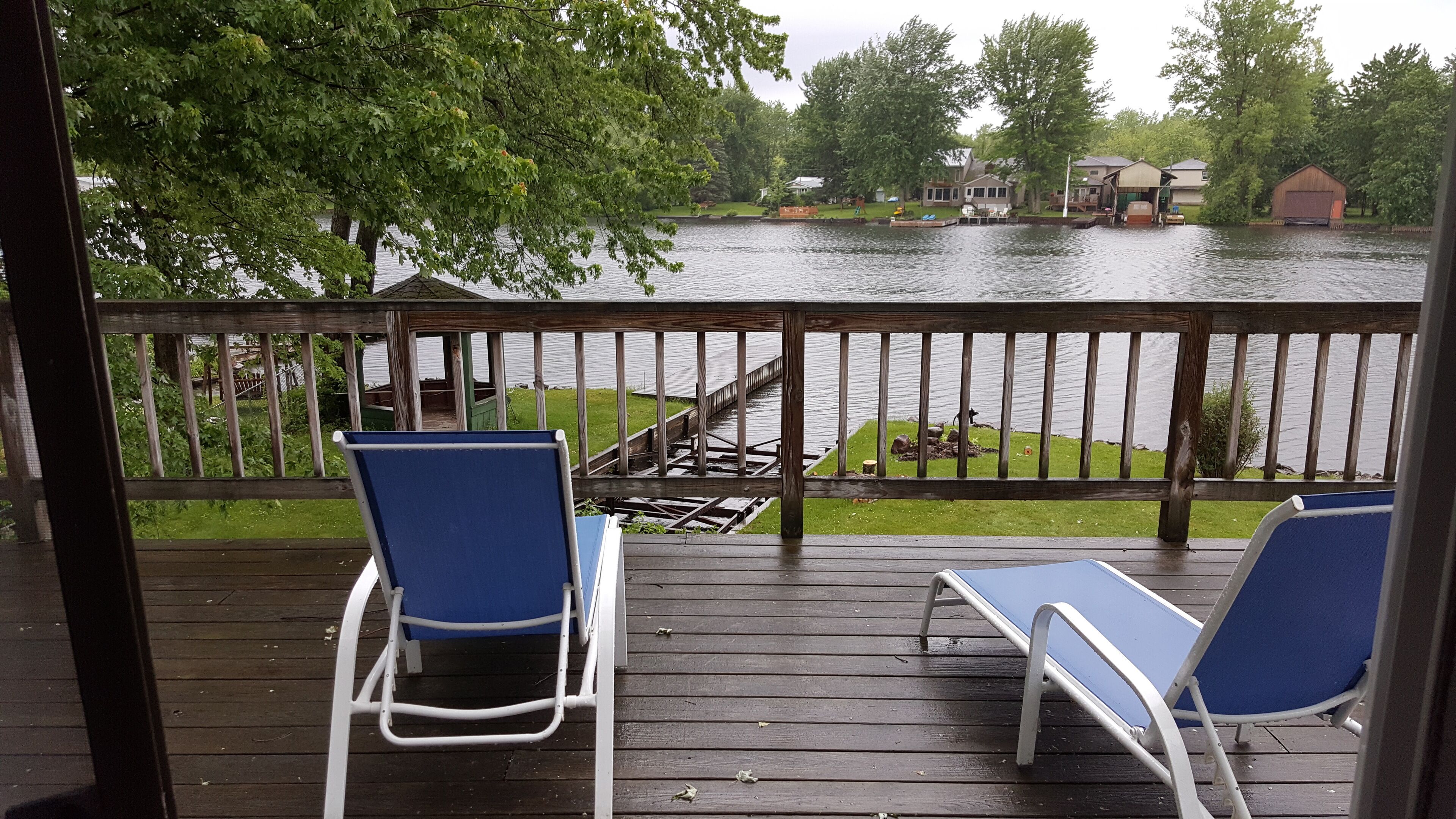 A wooden deck with two blue chairs and a view of a lake.
