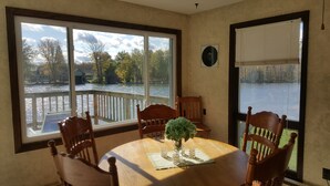 A dining area with a large window overlooking a river, a wooden table, and chairs.