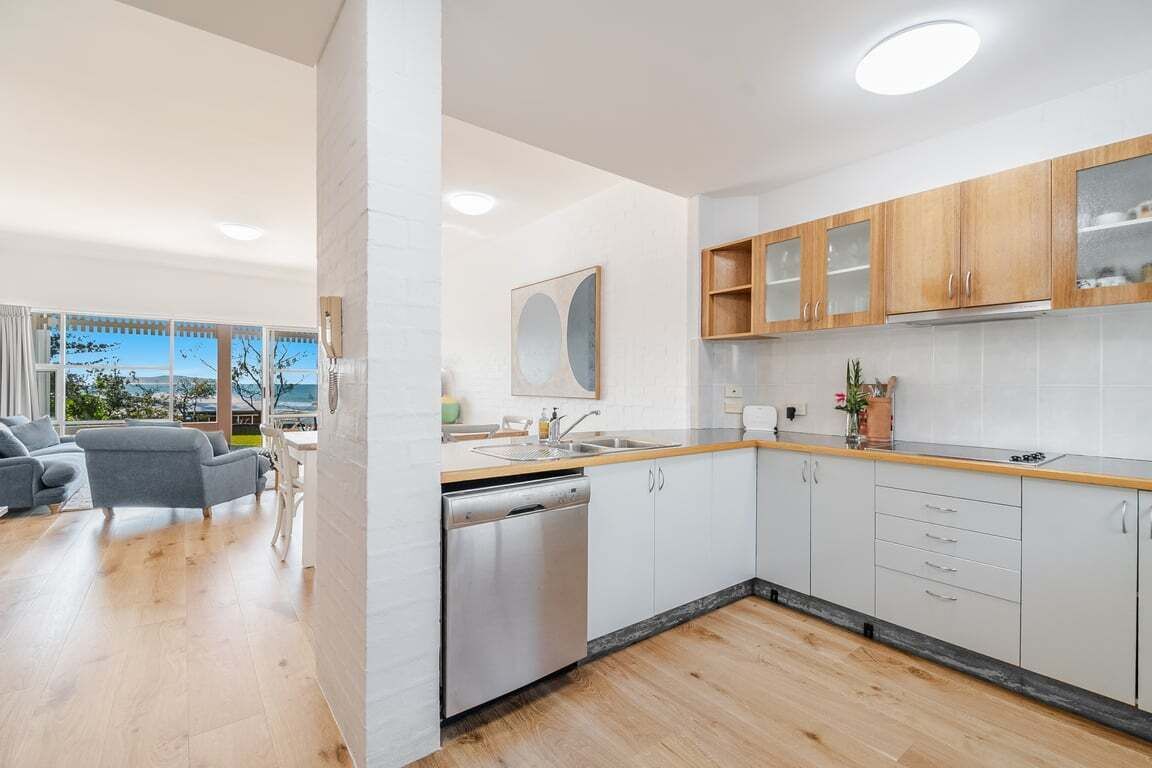 A modern kitchen with white cabinets, a dishwasher, and a view to the outside.