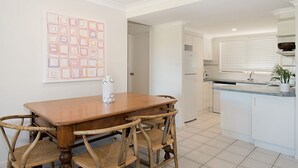 Een moderne keuken met witte kasten, een houten eettafel en een zeshoekige vaas.