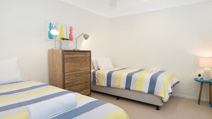 Een hotelkamer met twee bedden, een houten dressoir, een klein tafeltje met een lamp en een plafondventilator.