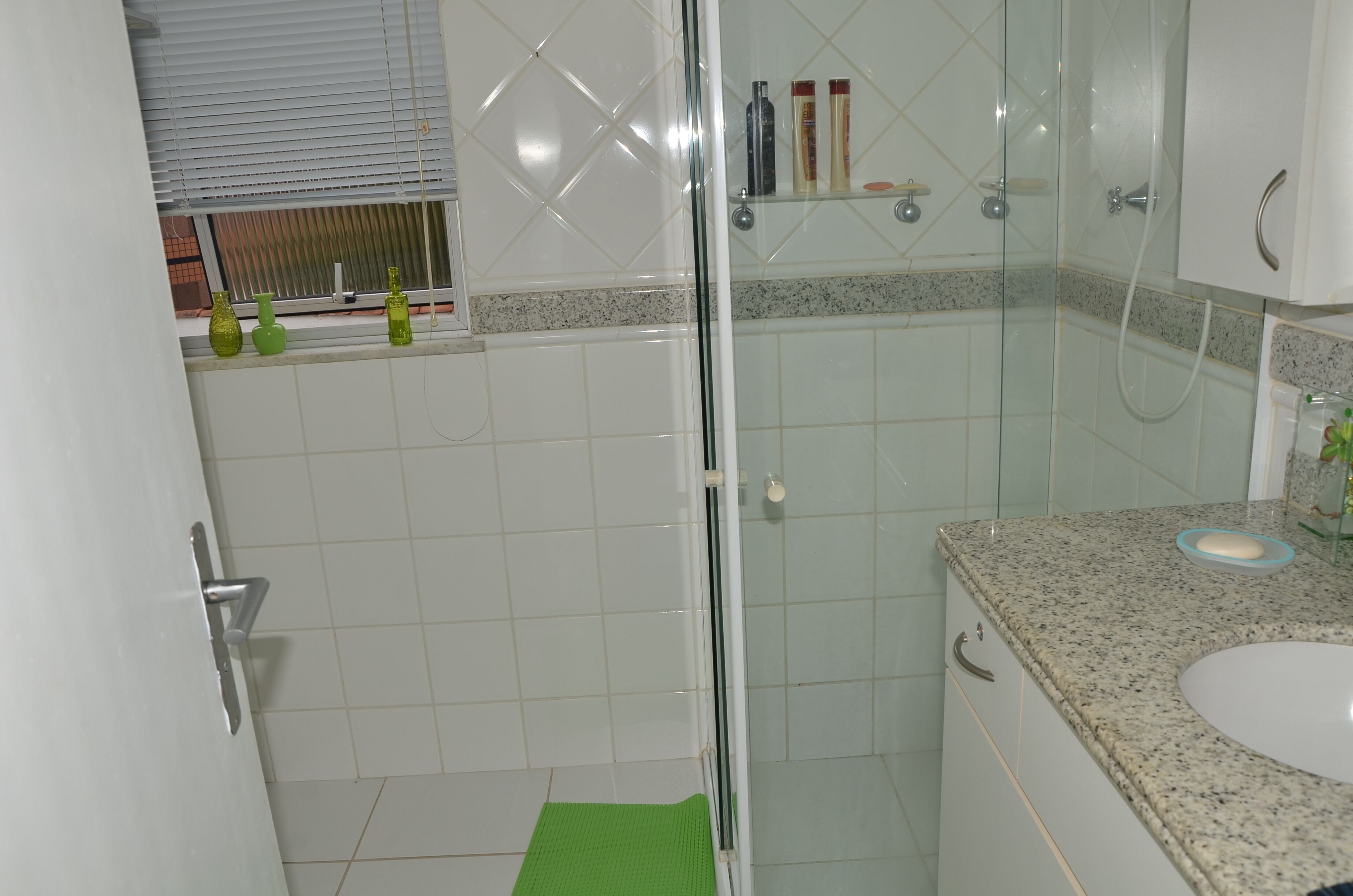 A bathroom with a glass shower enclosure, a white sink, and a green bath mat.