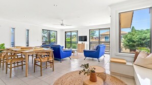 A spacious living area with a dining table, blue sofas, and a large window offering a view of the outdoors.