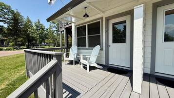 Une terrasse en bois avec deux chaises Adirondack et une table, une porte blanche et un drapeau.