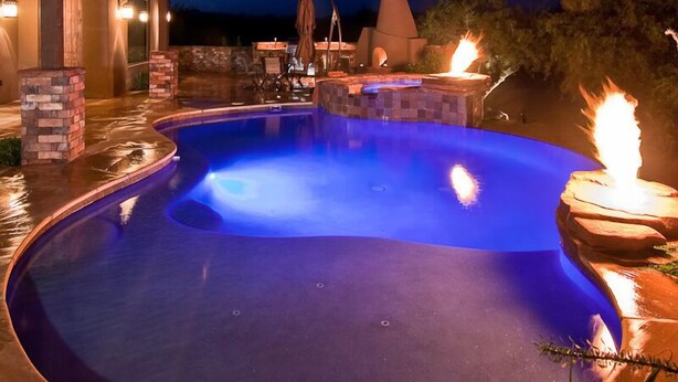Une piscine à bordures courbes, entourée d’une terrasse en pierre et d’une pergola en bois.