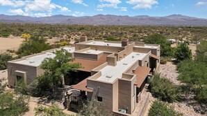 Un bâtiment moderne doté de plusieurs toits plats, entouré d’une végétation désertique et avec des montagnes en arrière-plan.