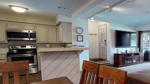 A compact kitchen with modern appliances, a dining area with wooden furniture, and a living room with a flat-screen TV. - Snowcreek Resort Vacation Rental 611 (Mammoth Lakes)