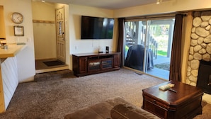 A living room with a large TV, a fireplace, and a sliding glass door leading to a deck. - Snowcreek Resort Vacation Rental 611 (Mammoth Lakes)