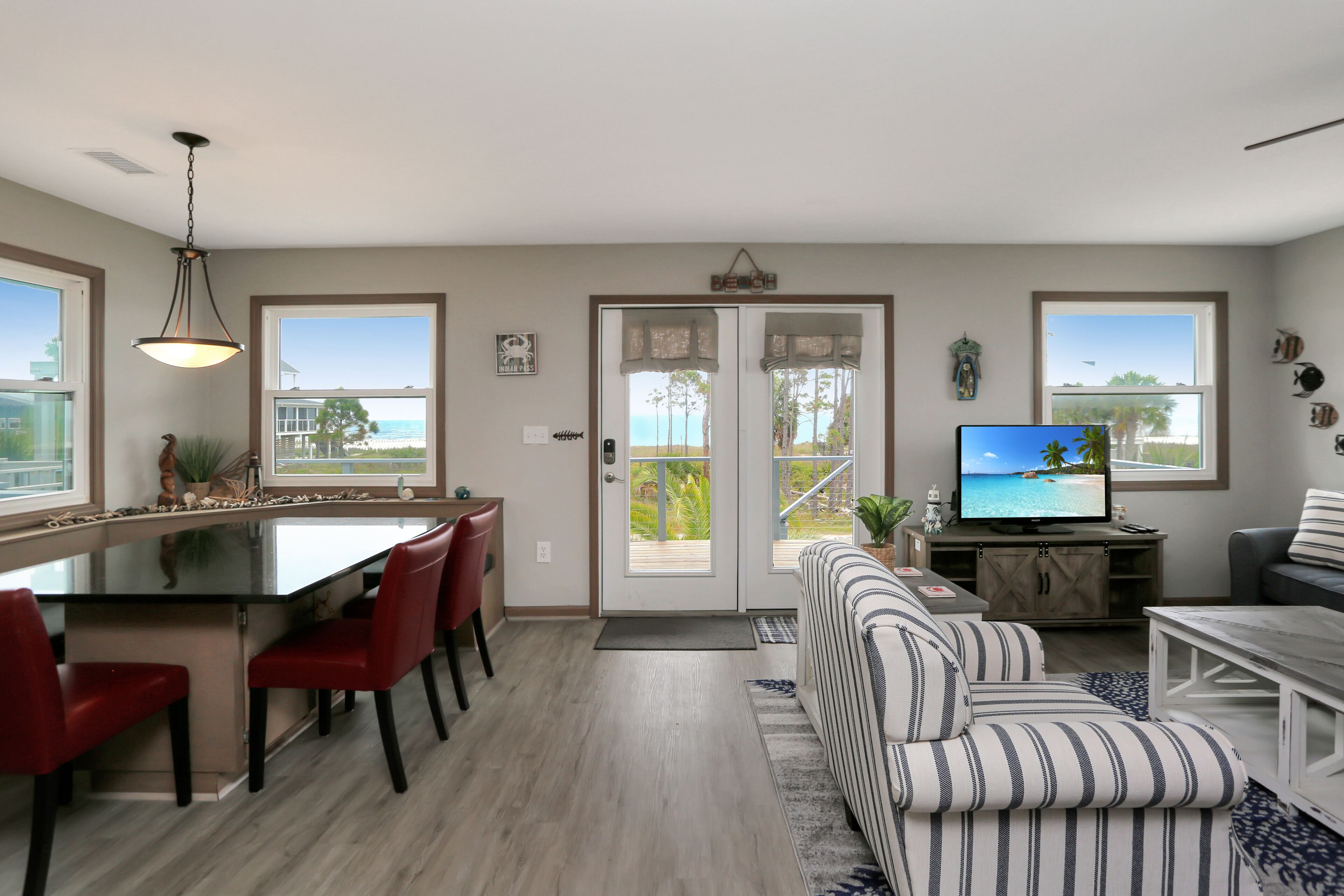 A modern living room with a large TV, a striped sofa, and a dining area with red chairs.