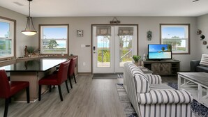 En moderne stue med et stort fjernsyn, en stribet sofa og et spiseområde med røde stole.