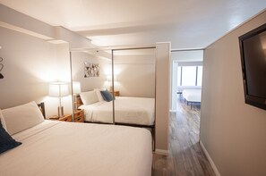 A hotel room with two beds, a sliding door closet, a TV, and a view of the hallway.