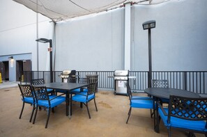 Un patio al aire libre con mesas, sillas, una parrilla y un bote de basura.