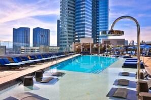 Piscina infinita en la azotea con sillas de descanso y vistas a edificios altos.
