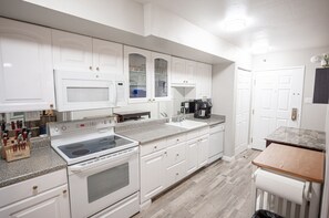 A modern kitchen with white cabinetry, a built-in microwave, a stove, and a coffee maker.