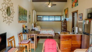 A spacious living area with a ceiling fan, a dining table with chairs, a sofa, a TV, and a kitchen area with a refrigerator.