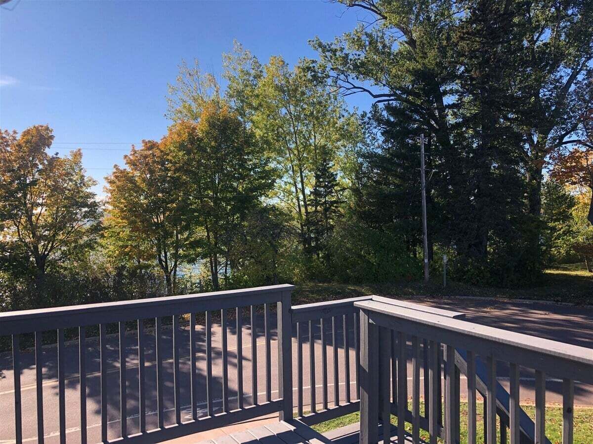 A wooden deck with a metal railing overlooking a road with trees and a clear sky.
