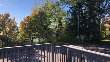 A wooden deck with a metal railing overlooking a road with trees and a clear sky.