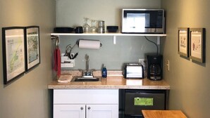 Una kitchenette compacta con microondas, tostadora, cafetera y un refrigerador pequeño.