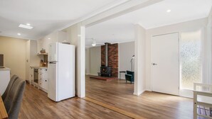 Eine moderne Küche mit weißen Geräten, ein Essbereich mit Tisch und Stühlen sowie ein Wohnbereich mit Kamin und Sofa.