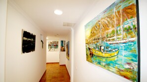 Ein Korridor mit Fliesenboden und Wänden, die mit verschiedenen Kunstwerken geschmückt sind, darunter ein auffälliges Gemälde eines Segelboots.