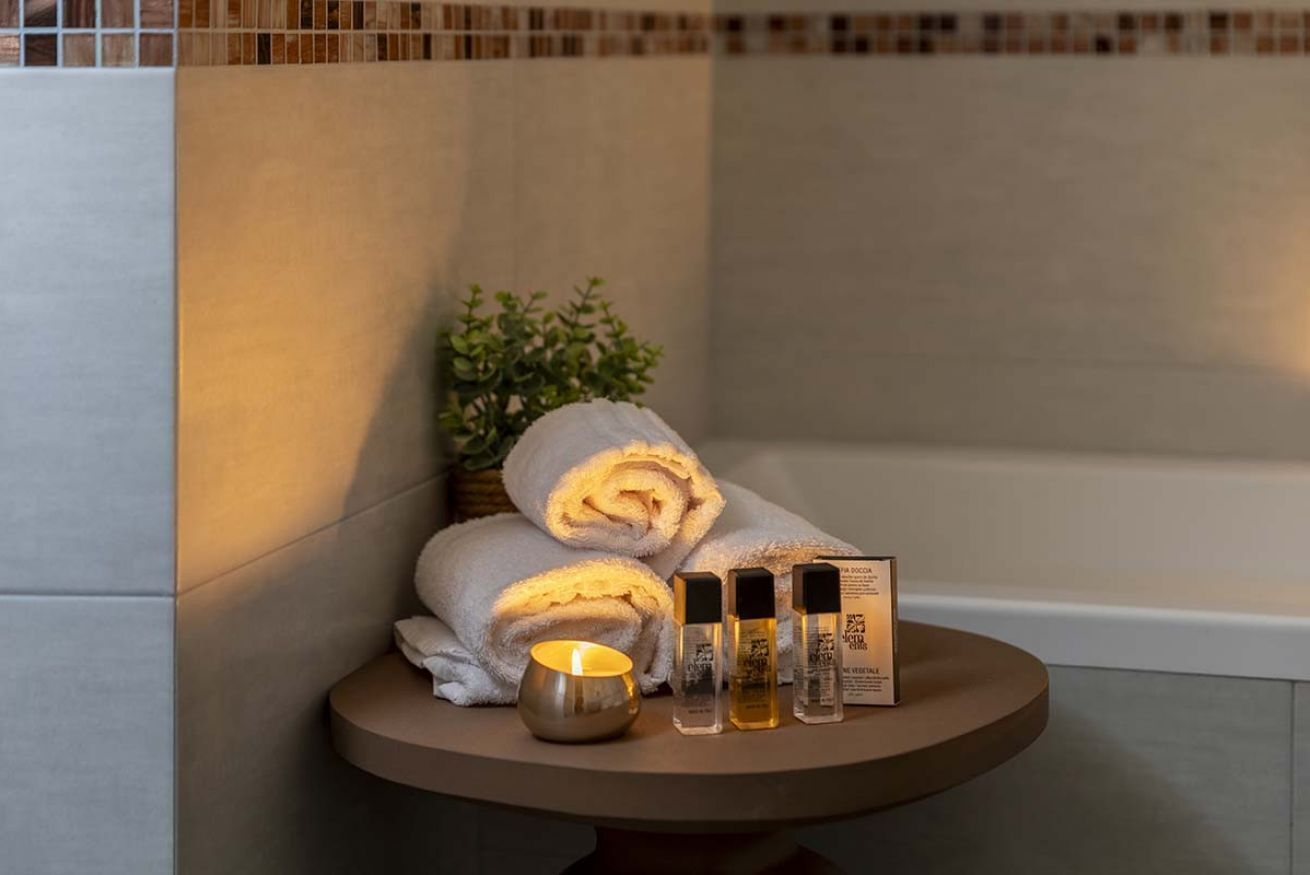 Ein Badezimmer mit einer Badewanne, einem kleinen Tisch mit zusammengerollten Handtüchern, einer Kerze und Pflegeprodukten.
