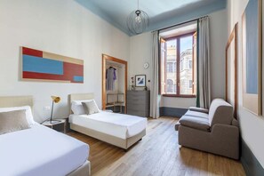 Une chambre d’hôtel avec deux lits, un canapé, un bureau et une grande fenêtre donnant sur des immeubles.