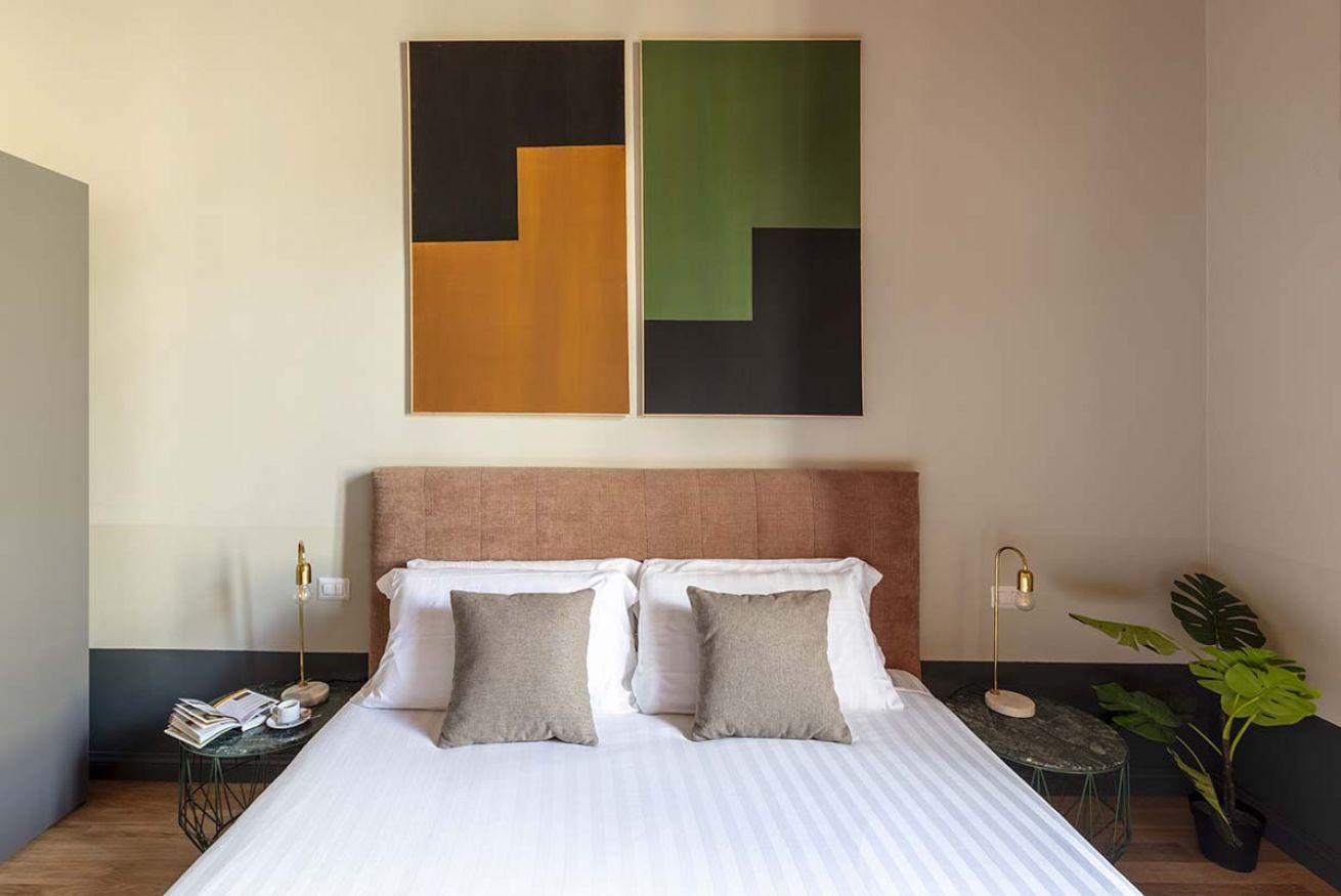 A hotel room with a large bed, two bedside tables, a potted plant, and abstract art on the wall.