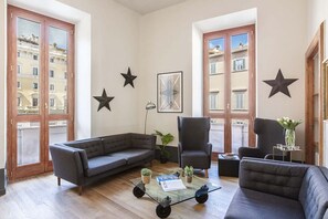 Un salon moderne avec un canapé gris, deux fauteuils, une table basse en verre et des étoiles décoratives sur les murs.
