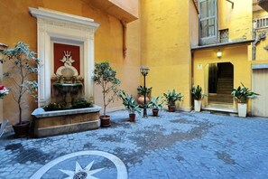 Ein Innenhof mit einem Brunnen, Topfpflanzen und einem Kopfsteinpflasterboden.