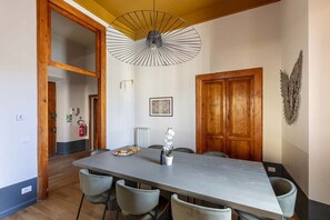 Un espace repas comprenant une longue table, des chaises, un ventilateur de plafond, un extincteur et une porte en bois.