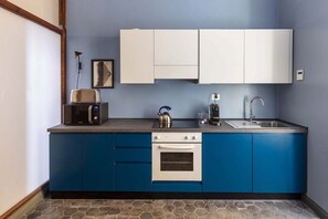 Une cuisine avec des meubles de rangement bleus, un four à micro-ondes, une bouilloire et un évier.