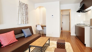 A modern living room with a sofa, a coffee table, and a kitchen area with a refrigerator and microwave. - Condominium･yuyuki (Yomitan)