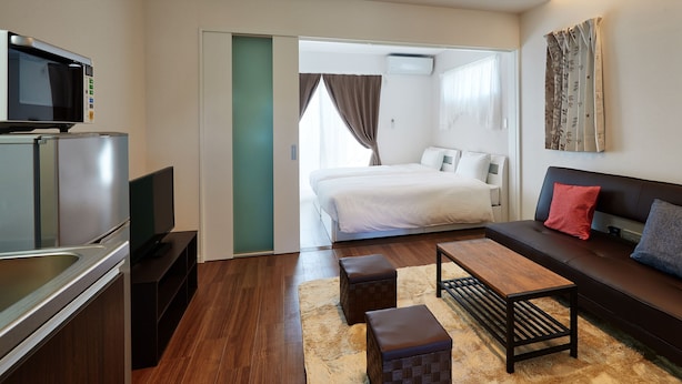 A modern hotel room with a kitchenette, a sofa, a coffee table, and a bed. - Condominium･yuyuki (Yomitan)
