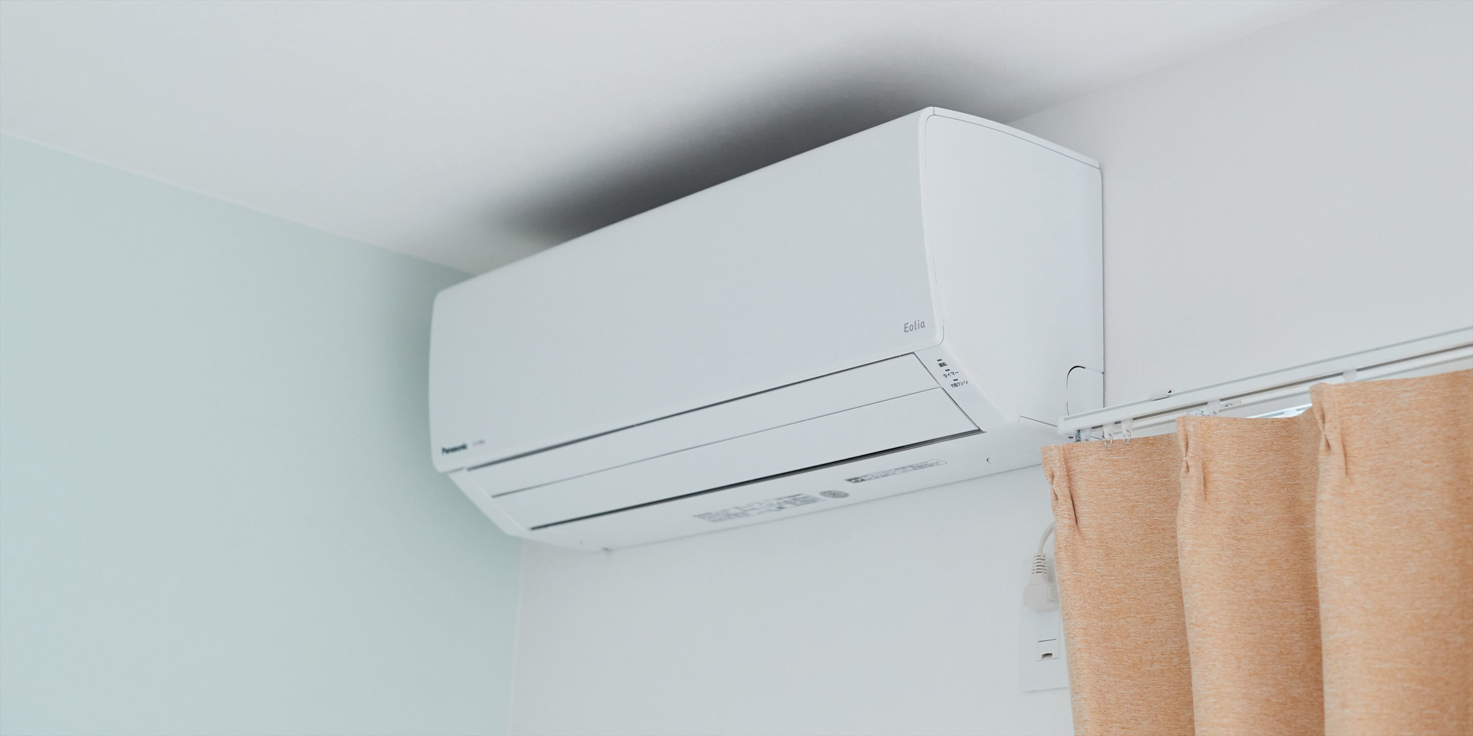 A white air conditioning unit mounted on a wall in a room with light blue walls and a brown curtain.