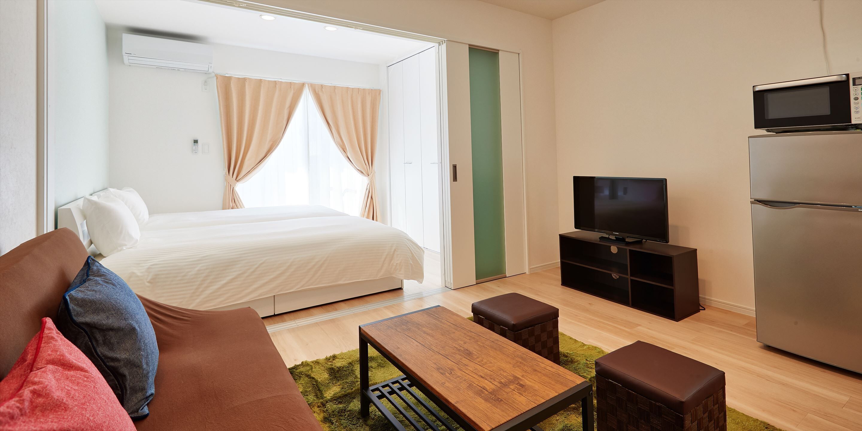 A modern hotel room with a bed, a TV, a refrigerator, and a wooden coffee table.
