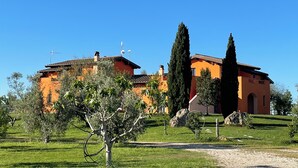 A large orange building with a tiled roof, surrounded by greenery and a clear blue sky.