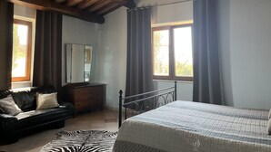A bedroom with a wooden ceiling, a bed, a dresser, a mirror, and two windows with curtains.