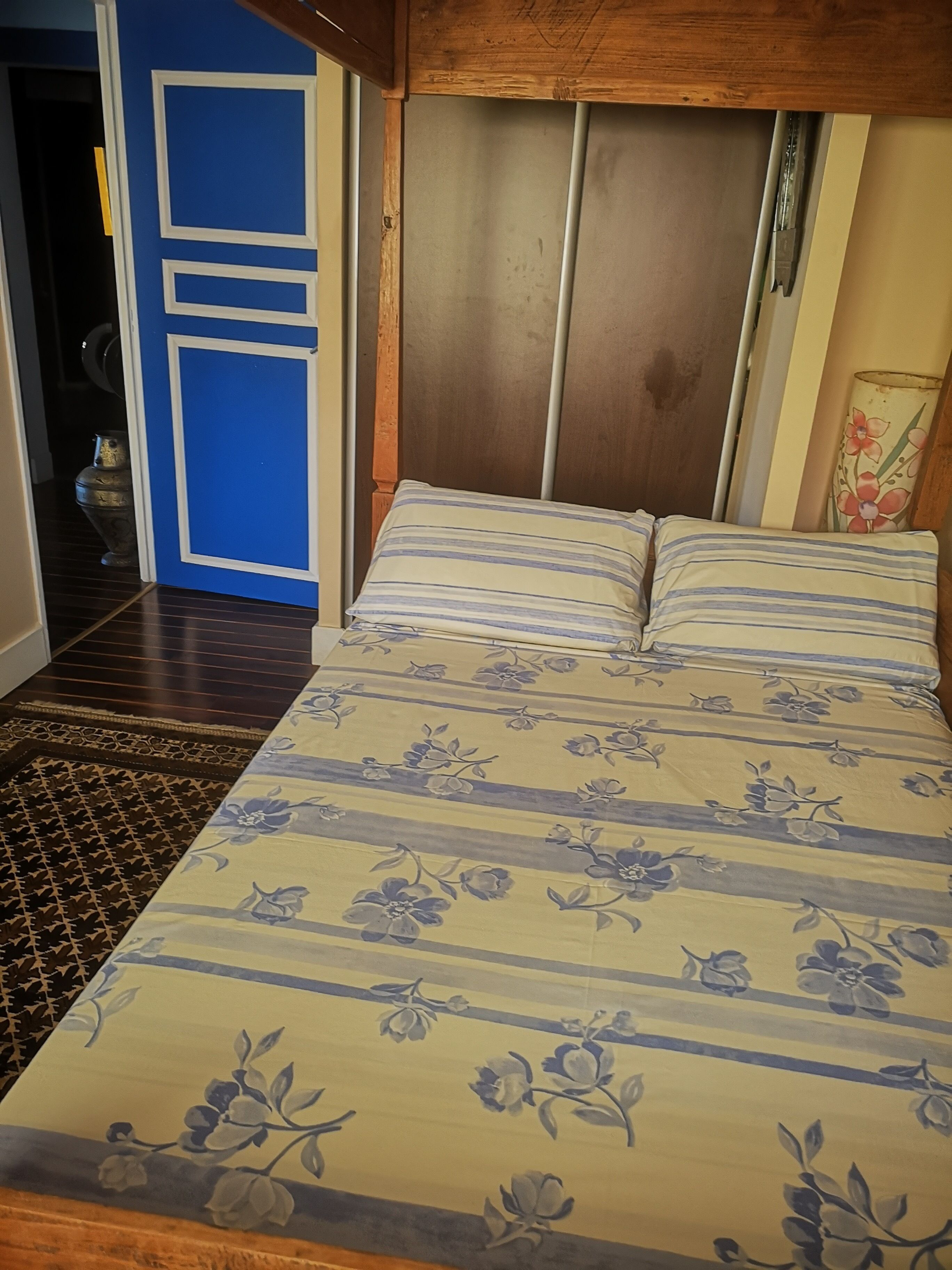 Ein Bett mit blumigem Bettzeug, einem Holzkopfende und einer blauen Tür im Hintergrund.