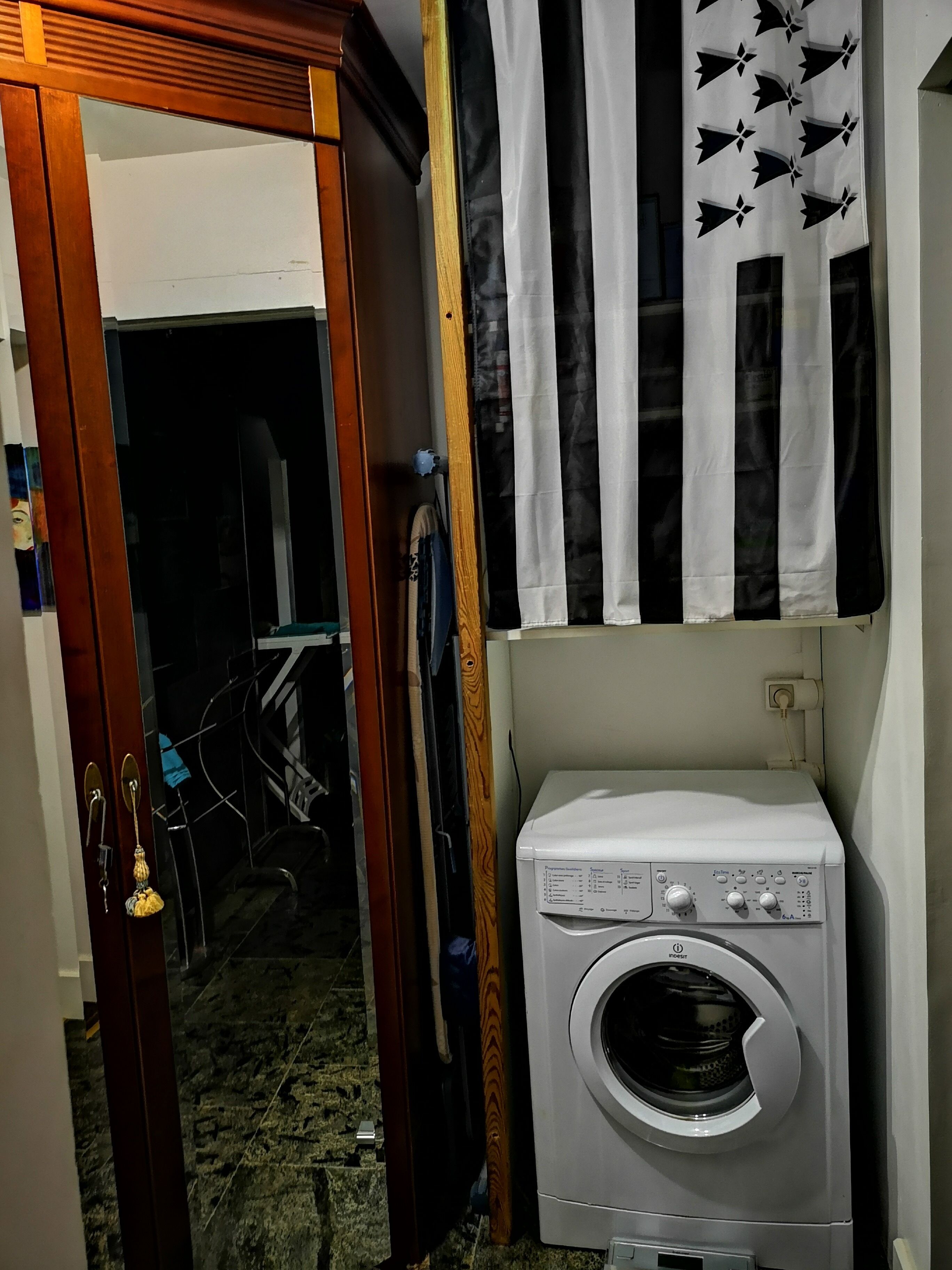 Uma lavanderia com máquina de lavar de abertura frontal, porta de madeira e cortina com padrão preto e branco.