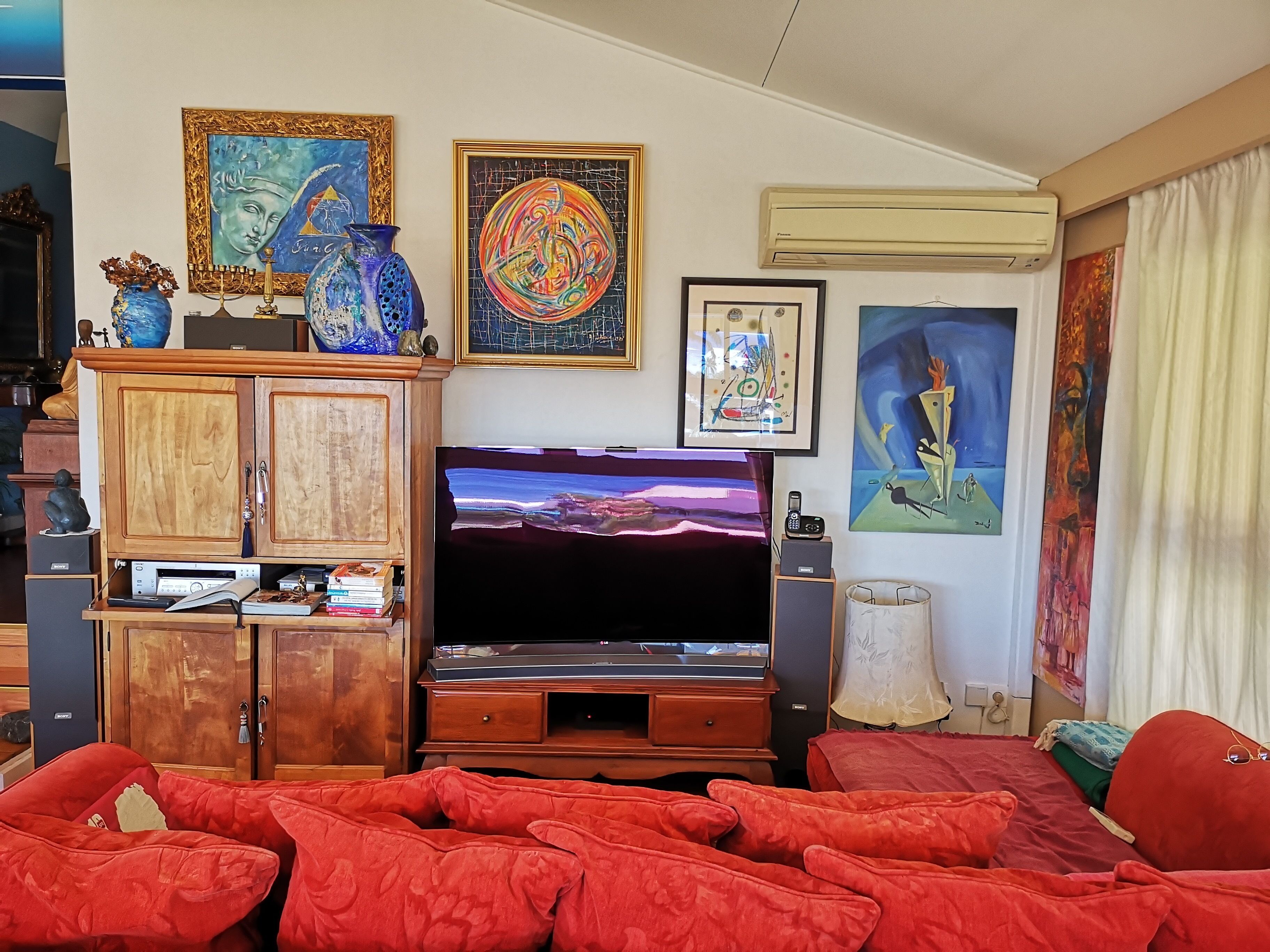 A living room with a flat-screen TV, wooden cabinets, red sofas, and various framed artworks on the walls.