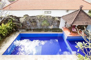 En swimmingpool med flisebelagte omgivelser, en stenvæg med beplantning og en lille pergola.