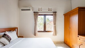 A bedroom with a bed, a wardrobe, a window with curtains, and an air conditioning unit. - Rumah Akira Seminyak (Seminyak)