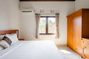 A bedroom with a bed, a wardrobe, a window with curtains, and an air conditioning unit. - Rumah Akira Seminyak (Seminyak)