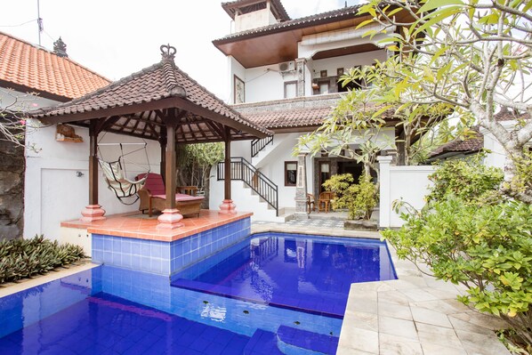 En swimmingpool med fliseterrasse, en pavillon og en trappe, der fører til en anden etage.