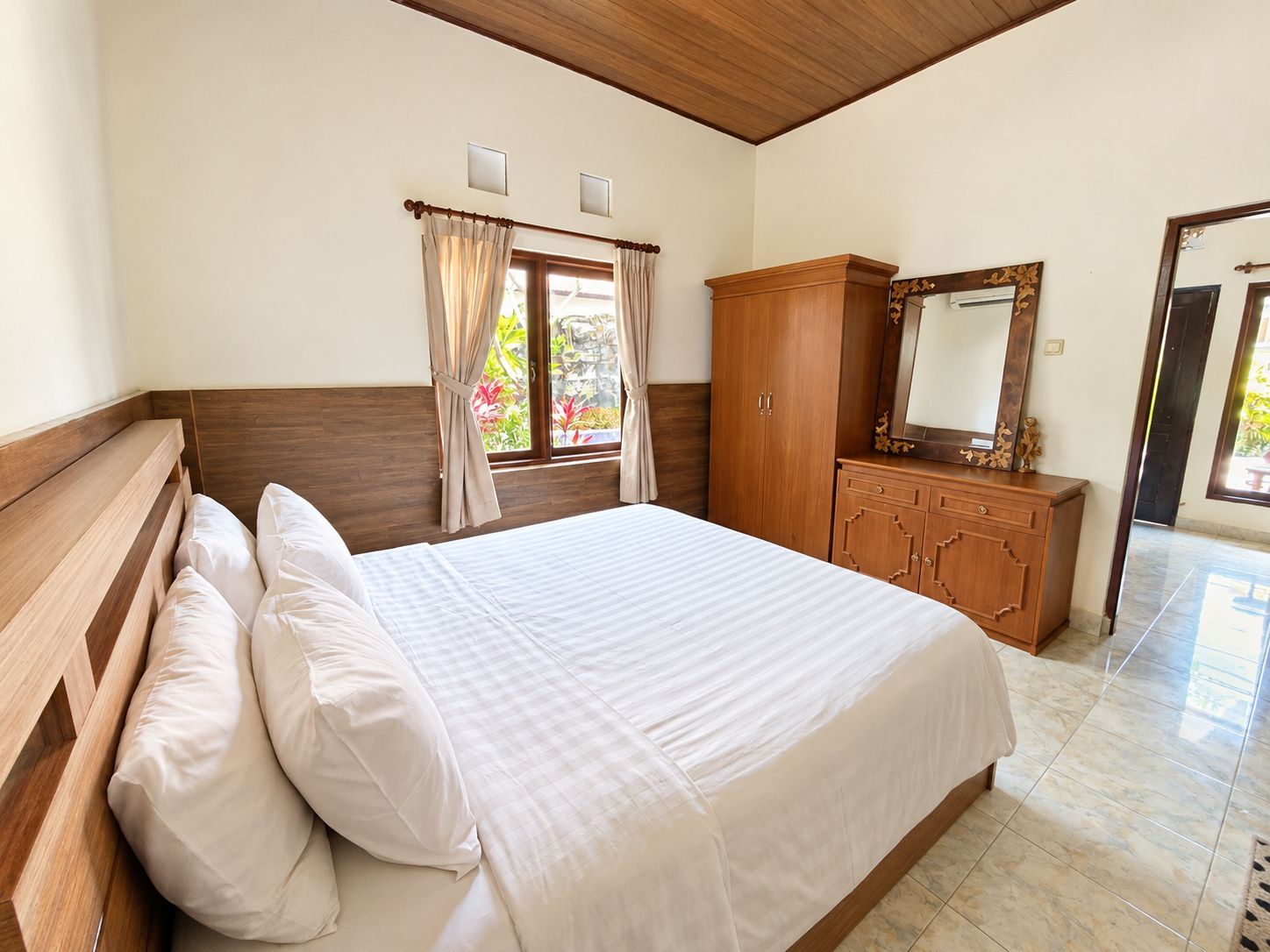 A bedroom with a wooden headboard, a large bed with white bedding, a wooden dresser, and a mirror.