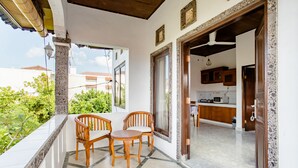 A balcony with two wooden chairs and a small table, a kitchen area with wooden cabinets, and a view of greenery. - Rumah Akira Seminyak (Seminyak)