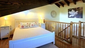 A bedroom with a wooden ceiling, a bed with floral pillows, a nightstand, a wall clock, and a staircase.