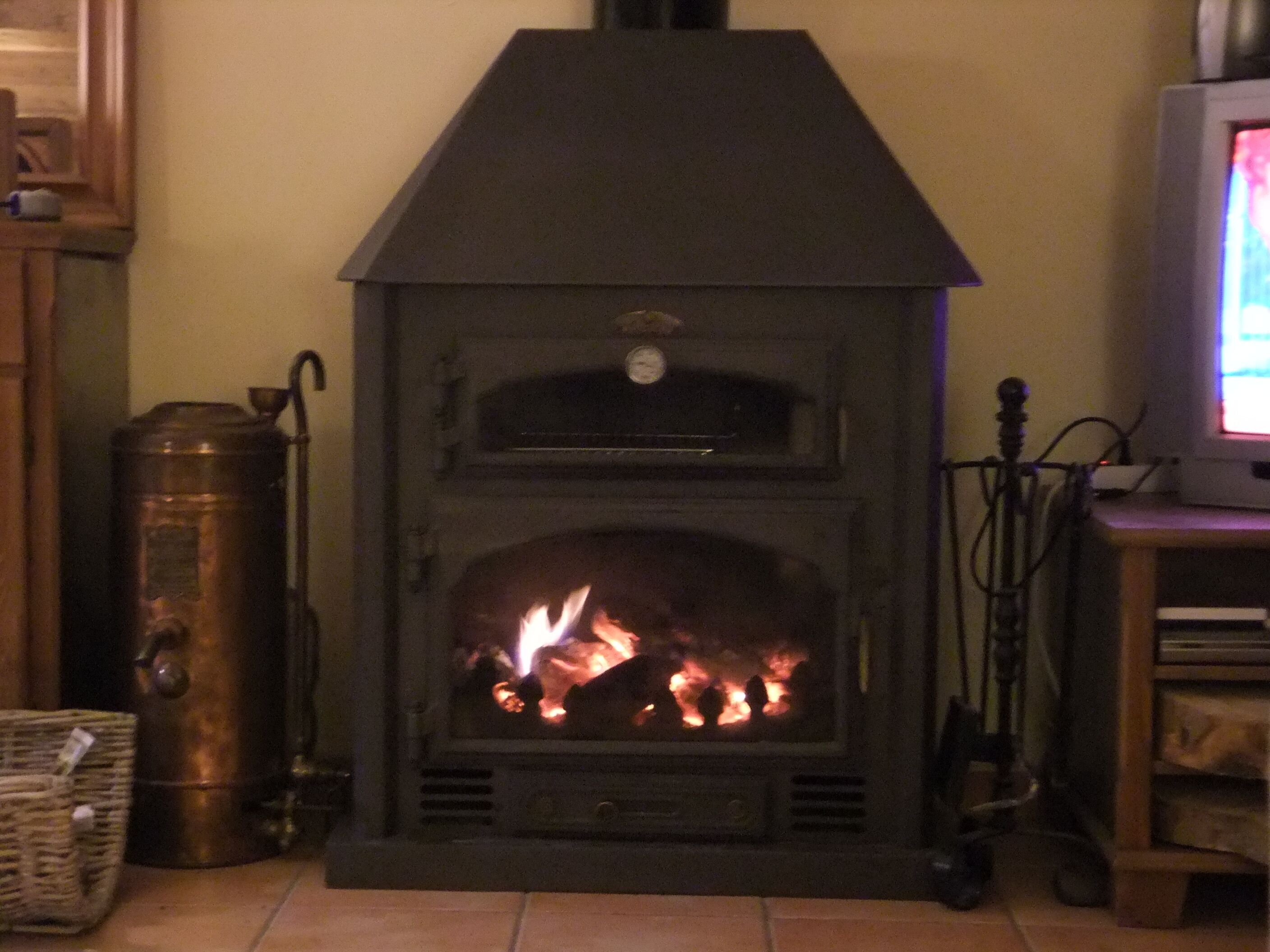 Una estufa de leña con chimenea, un televisor sobre un mueble bajo y una cesta de mimbre en el suelo.